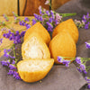 Three fried coxinhas with one cut open, surrounded by purple flowers on a dark surface.