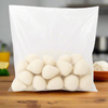 Transparent plastic bag filled with frozen mini Brazilian chicken coxinhas with Catupiry, teardrop-shaped and coated with a light breadcrumb layer, on a white background.