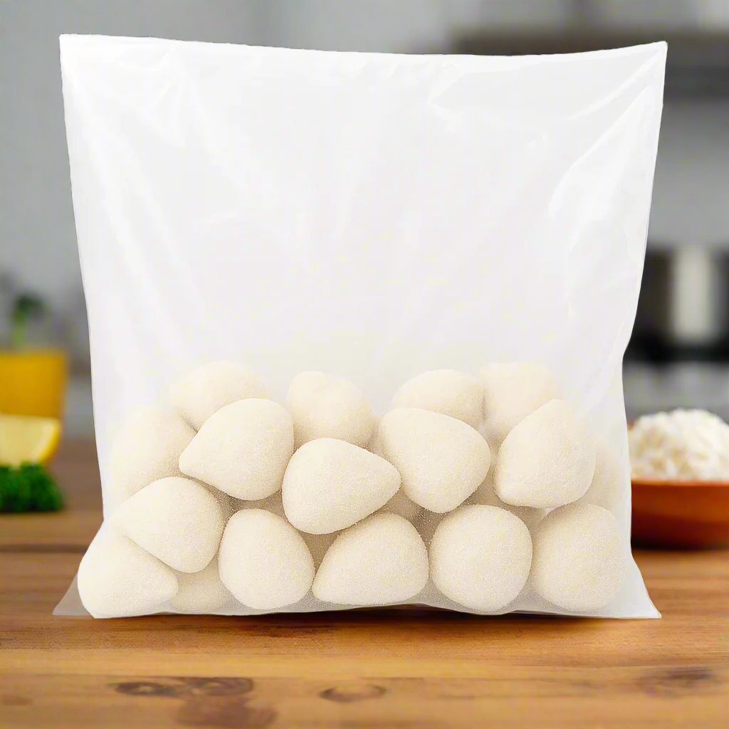 Transparent plastic bag filled with frozen mini Brazilian chicken coxinhas with Catupiry, teardrop-shaped and coated with a light breadcrumb layer, on a white background.